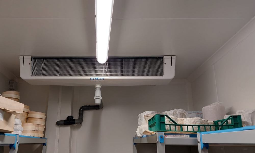 Évaporateur fixé au plafond d’une chambre froide, au-dessus d’étagères de fromages