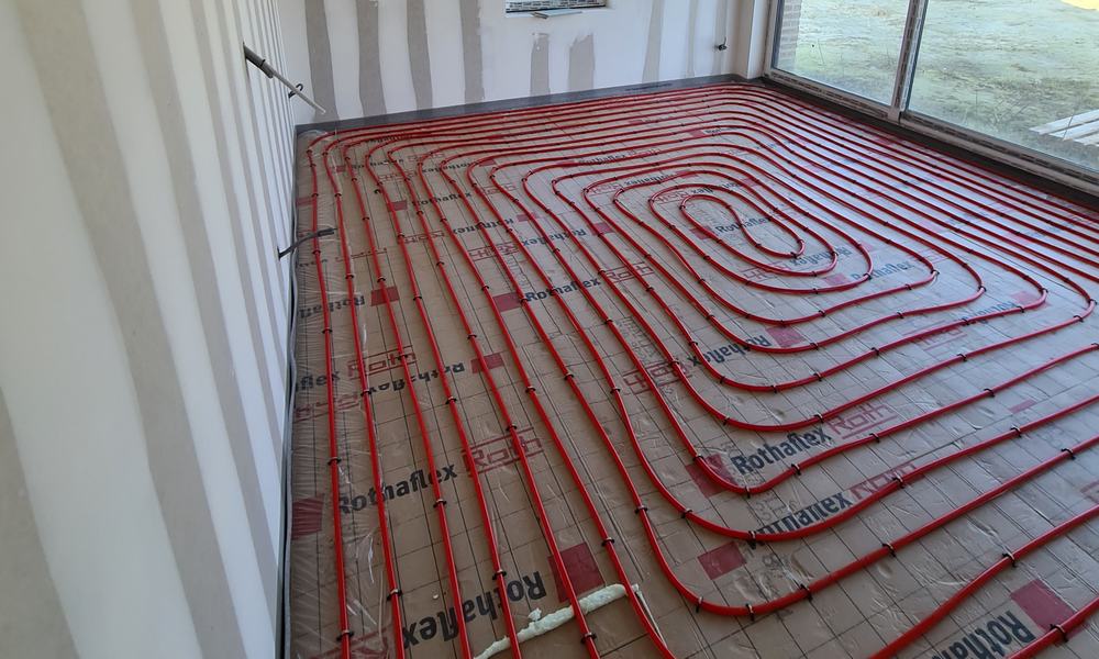 Tubes de plancher chauffant posés en spirale dans une pièce avec grande baie vitrée